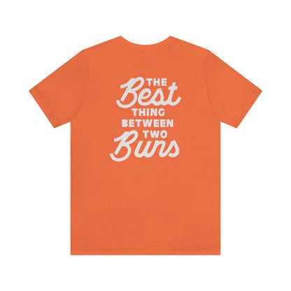 Orange short-sleeve cotton jersey tee featuring white text on the back that reads The Best Thing Between Two Buns.