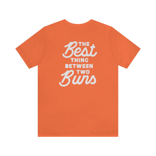 Orange short-sleeve cotton jersey tee featuring white text on the back that reads The Best Thing Between Two Buns.