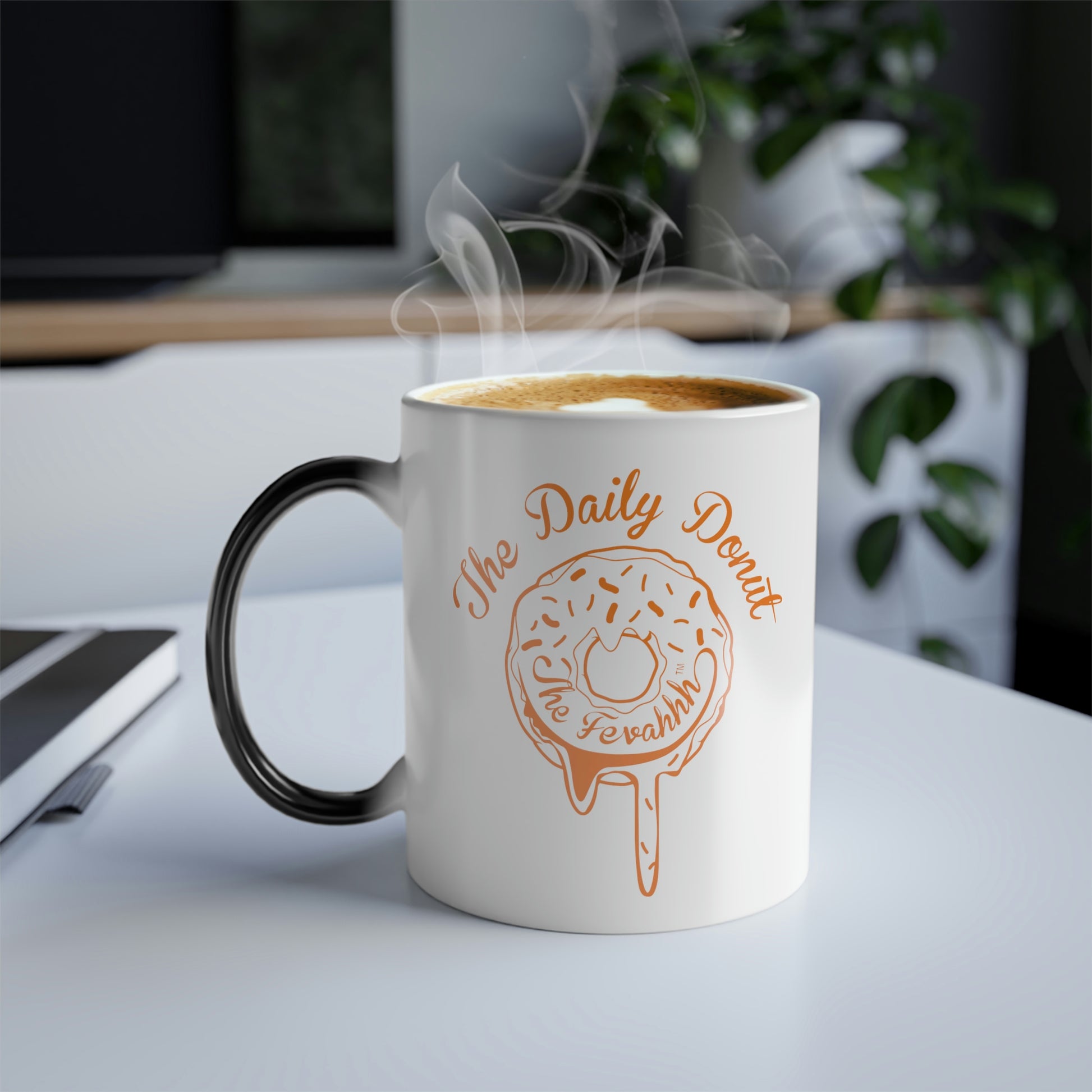 11oz ceramic heat-reactive mug with a white exterior, orange donut graphic, and black C-shaped handle on a desk.